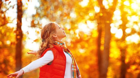 nő szétnyitott karral az őszi falevelek között