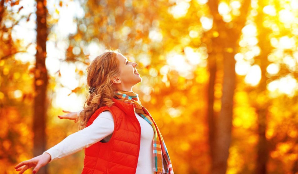 nő szétnyitott karral az őszi falevelek között