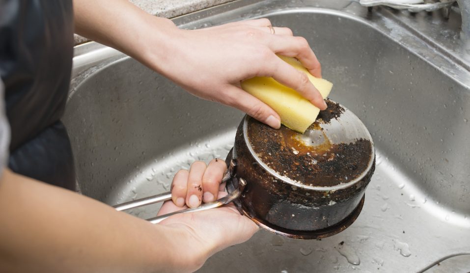 zsíros serpenyő alját mosogatja egy nő