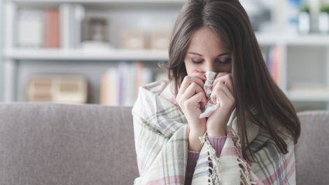 Egy nő otthon a kanapén fújja az orrát