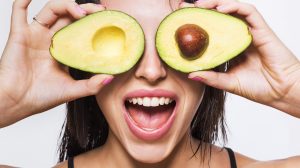 Egy nő félbe vágott avokádót tart a szeme elé
