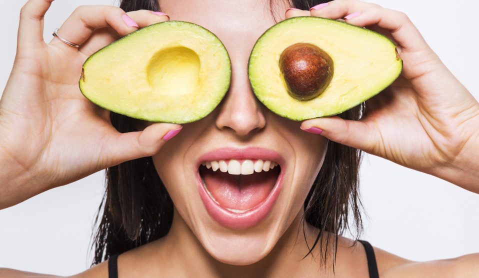 Egy nő félbe vágott avokádót tart a szeme elé