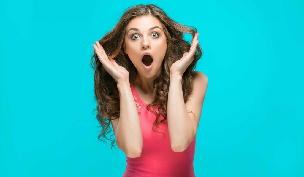Nő látványosan meglepődik a kék háttér előtt