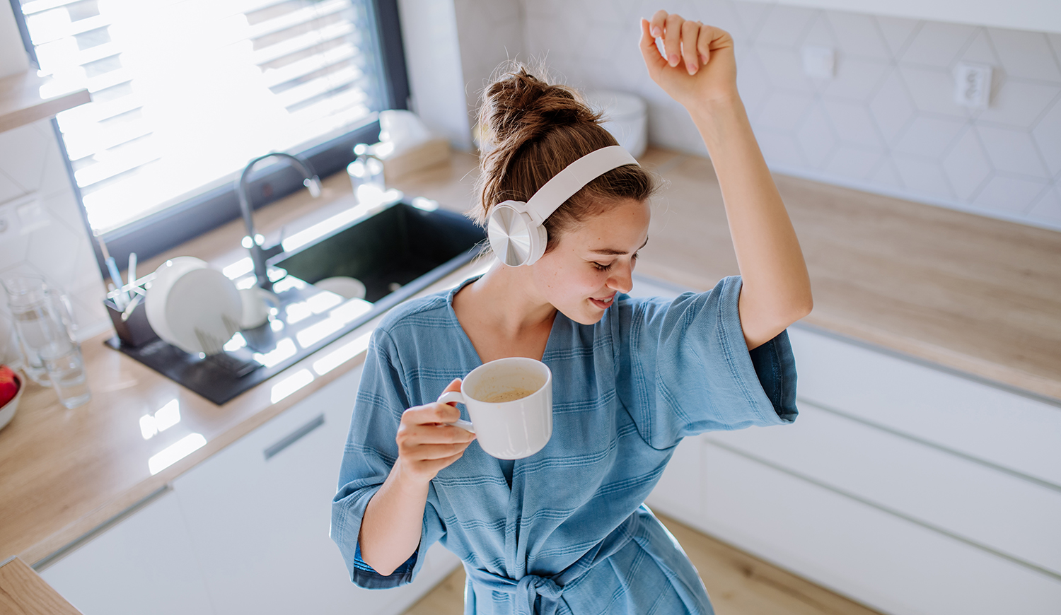 Fiatal nő élvezi a kávét és zenét hallgat reggel, a konyhában