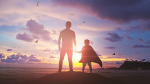 Fiú fogja az apja kezét a naplementében