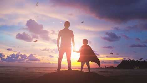 Fiú fogja az apja kezét a naplementében