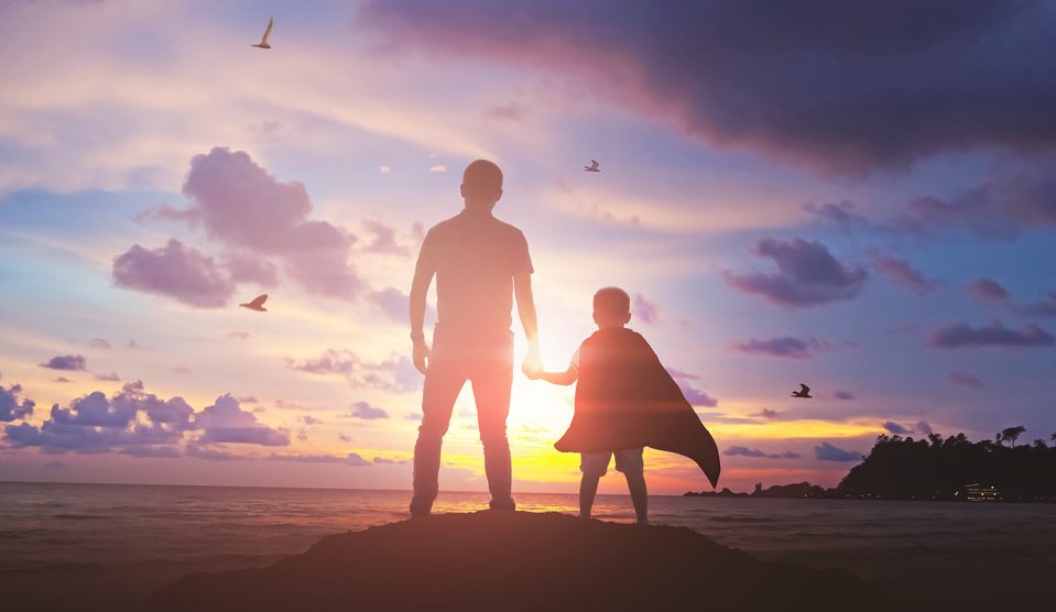 Fiú fogja az apja kezét a naplementében