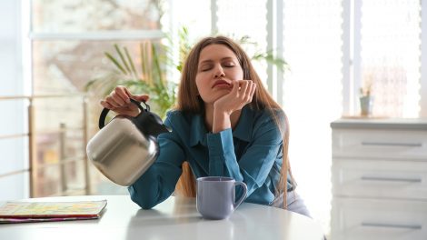 Álmos fiatal nő kávét önt a csészébe otthon