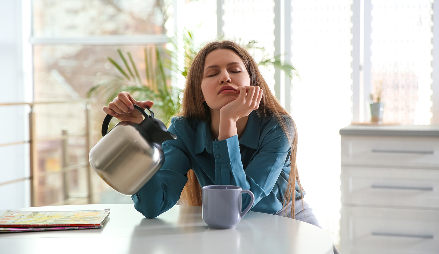 Álmos fiatal nő kávét önt a csészébe otthon