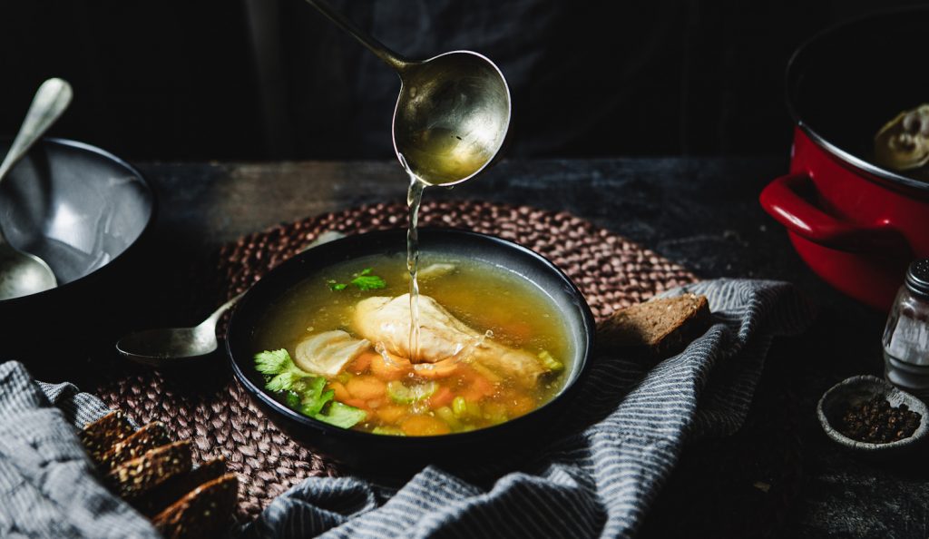 aranyló csirkehúslevest szed tányérba egy nő