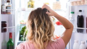 nő áll a hűtő előtt és vakarja a fejét