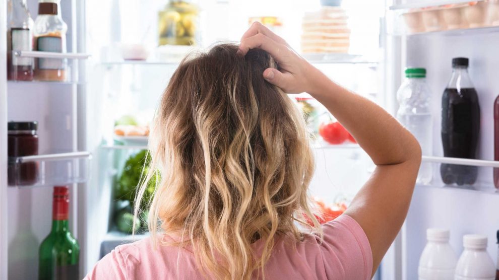nő áll a hűtő előtt és vakarja a fejét
