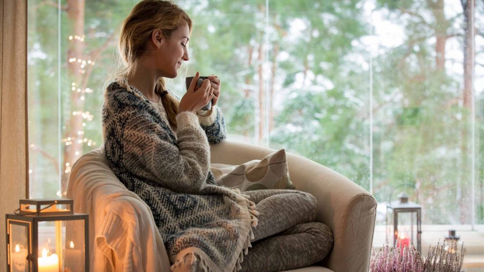 nő kávéval a kezében ül a fotelben