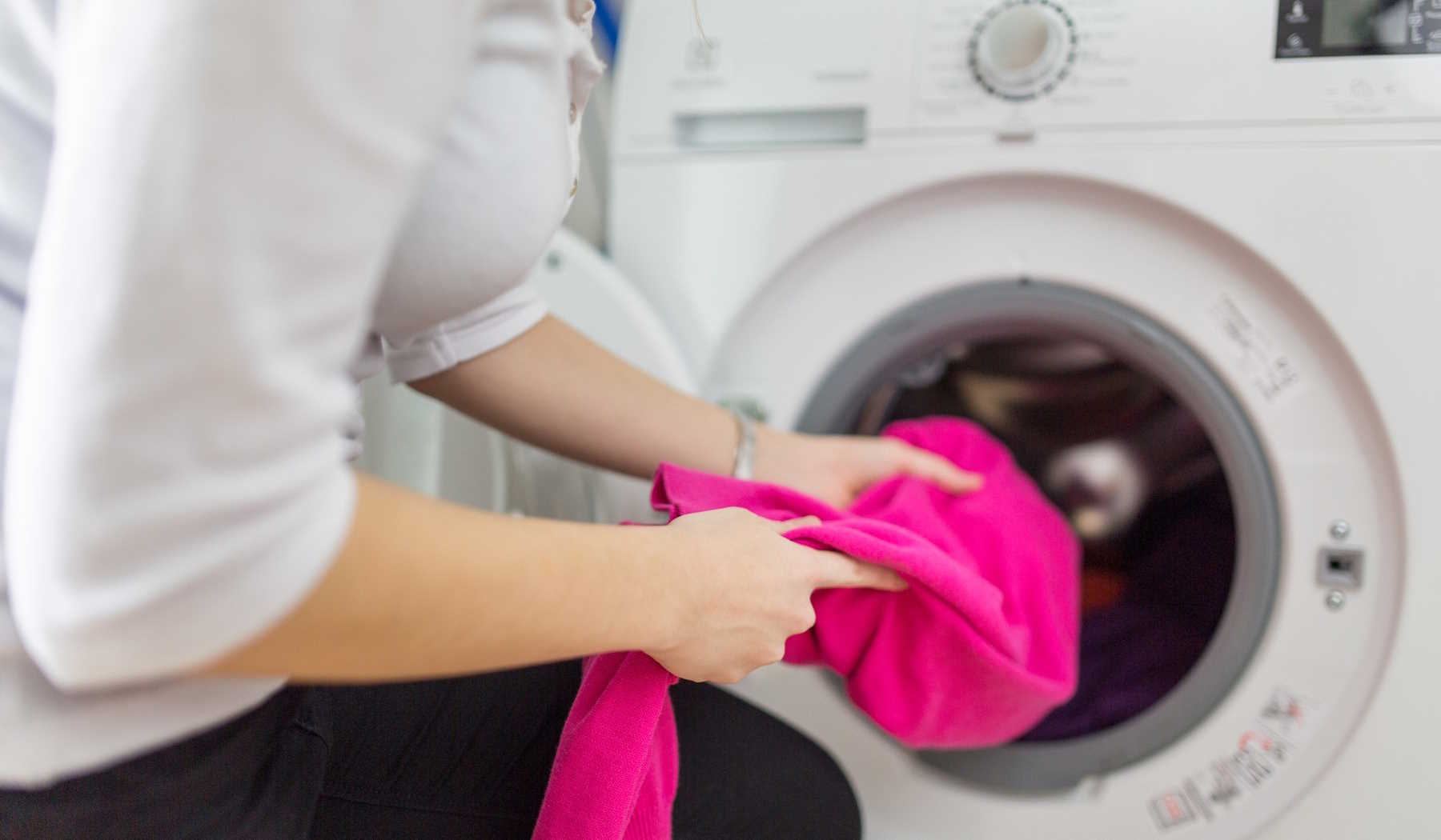 nő rózsaszín ruhát tesz a mosógépbe