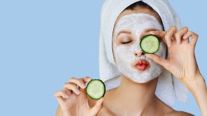 fiatal nő arcpakolásban, friss uborka szeleteket tartva az arca előtt