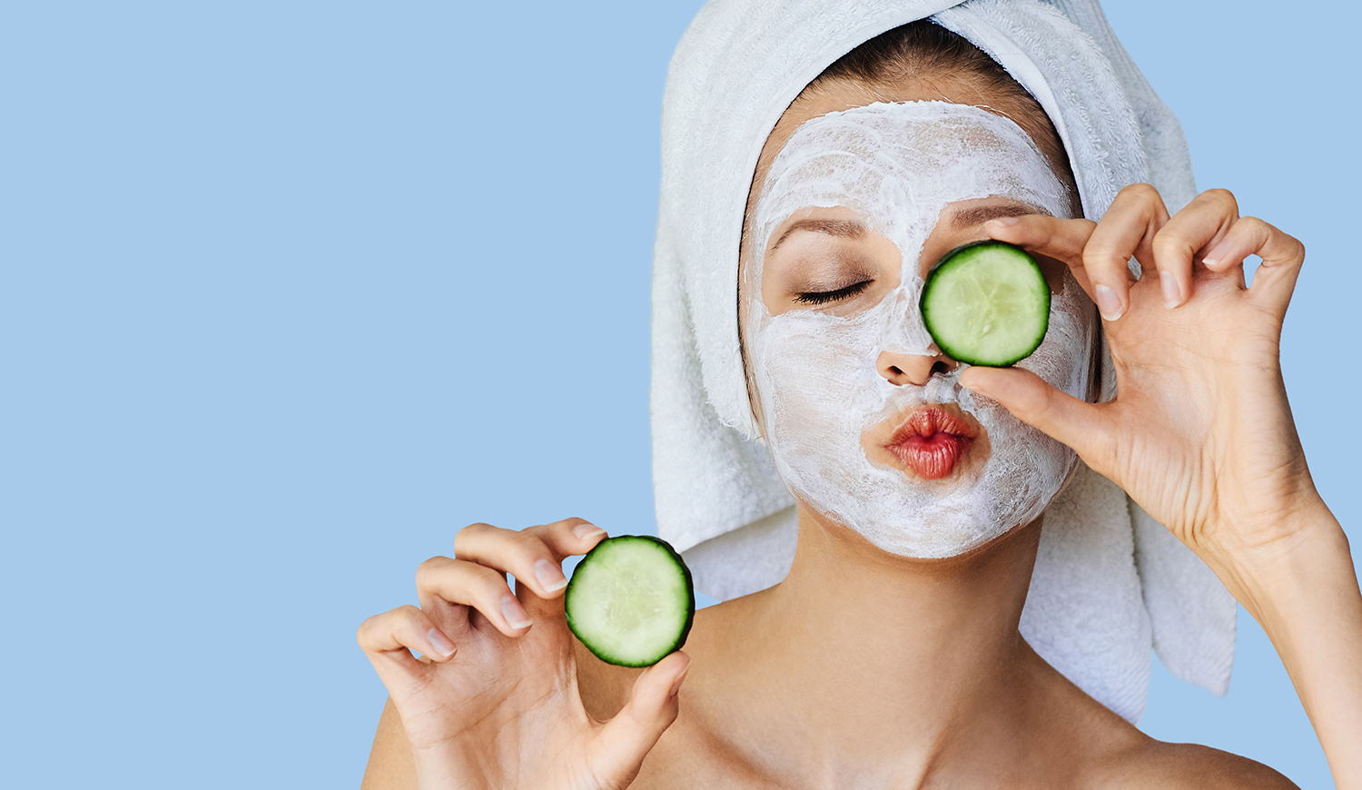 fiatal nő arcpakolásban, friss uborka szeleteket tartva az arca előtt
