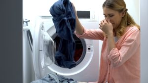 büdös mosógépből ruhákat vesz ki egy nő