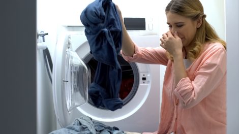 büdös mosógépből ruhákat vesz ki egy nő