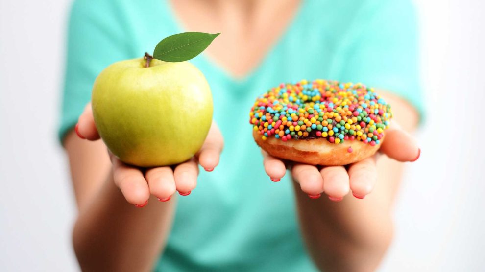 a nő a kezében tart egy almát és egy cukros fánkot