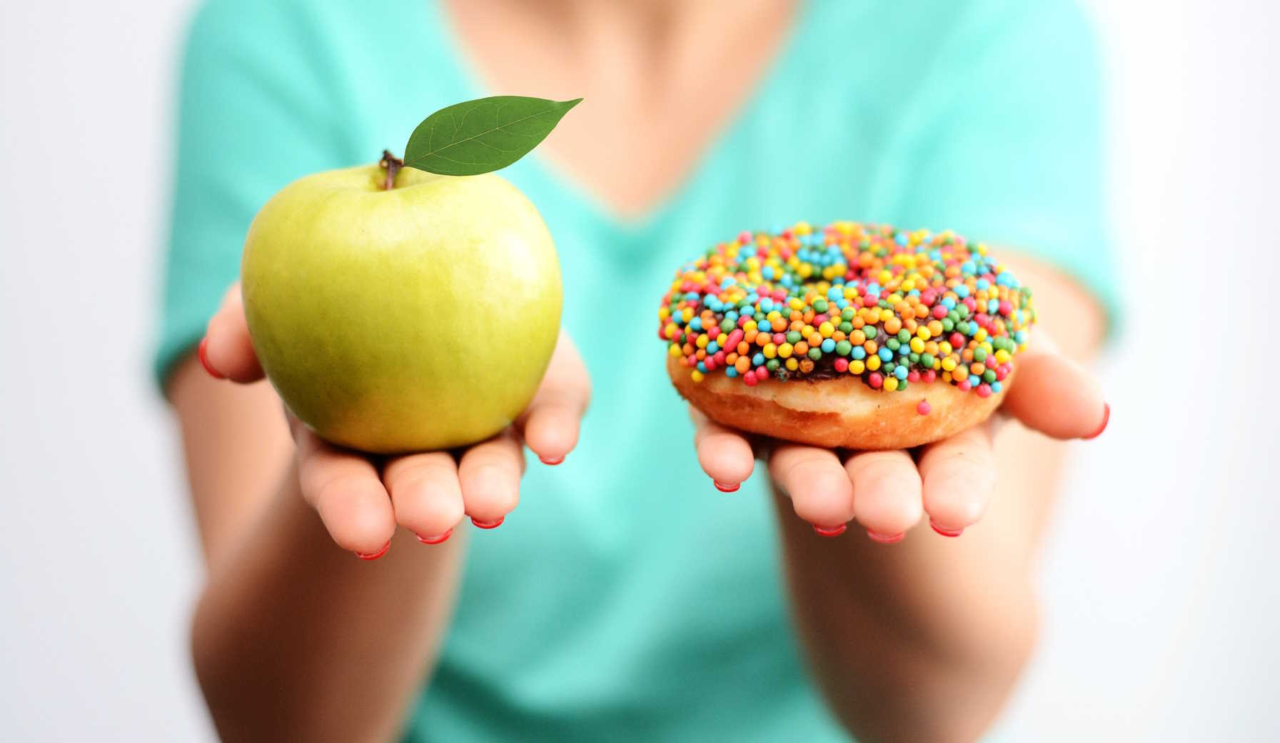 a nő a kezében tart egy almát és egy cukros fánkot