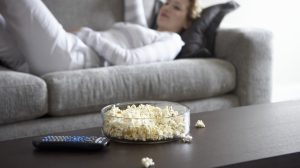 Egy nő fekszik a kanapén és popcorn van a dohányzóasztalon