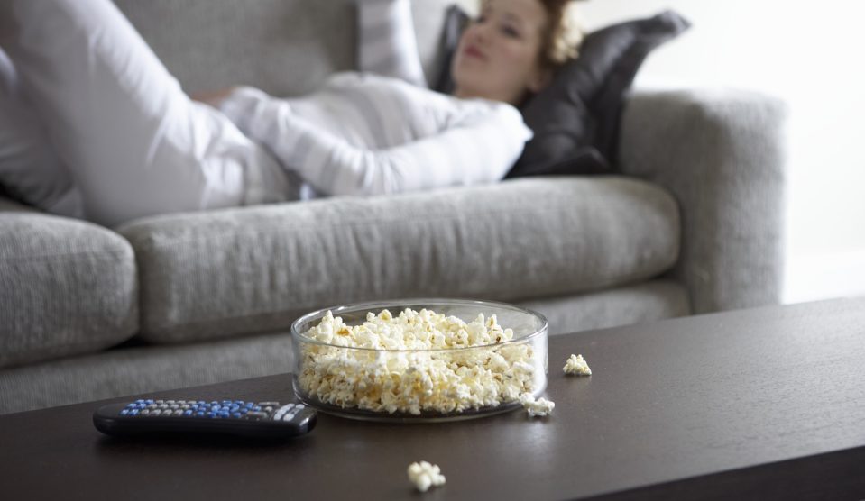 Egy nő fekszik a kanapén és popcorn van a dohányzóasztalon