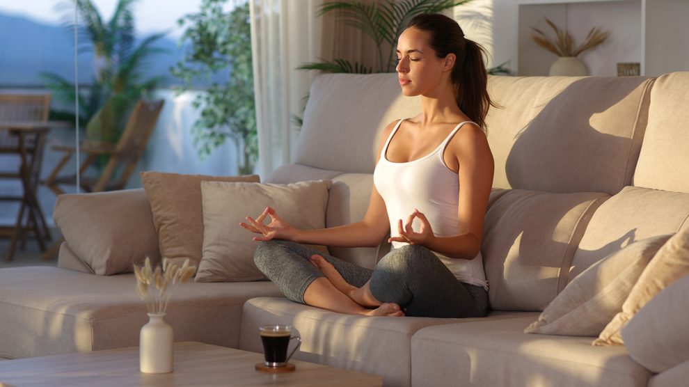 Fiatal nő jógázik és meditál a kanapén