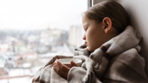 Szomorú kislány az ablakban ül teával a kezében