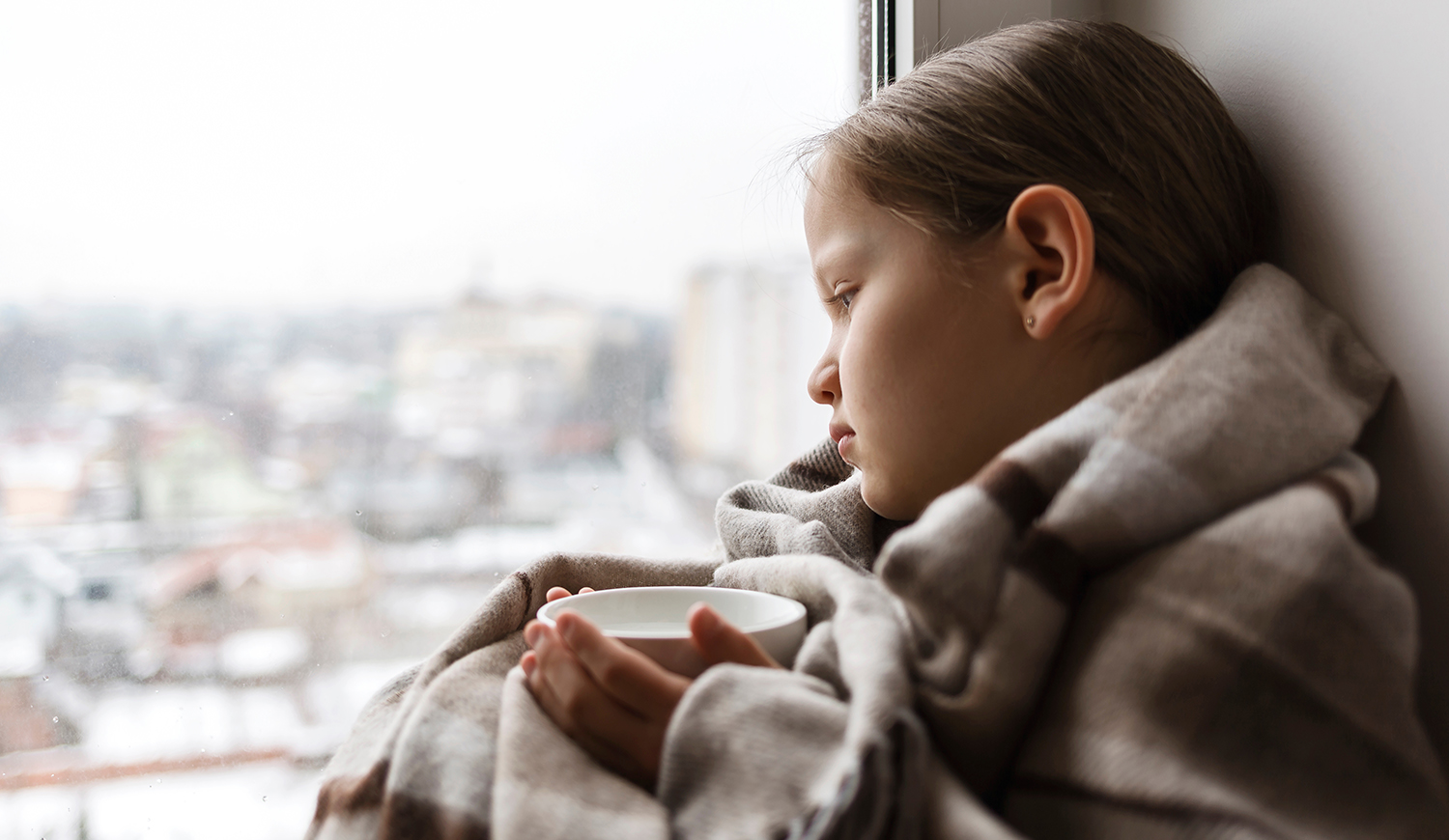 Szomorú kislány az ablakban ül teával a kezében