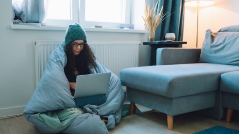 Egy nő leptopozik paplanba takarva a radiátornál