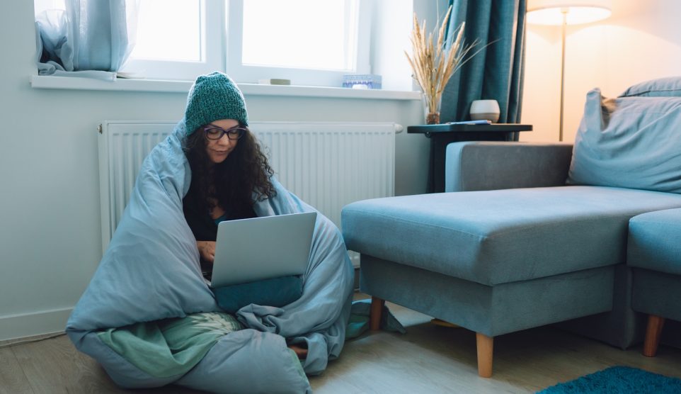 Egy nő leptopozik paplanba takarva a radiátornál