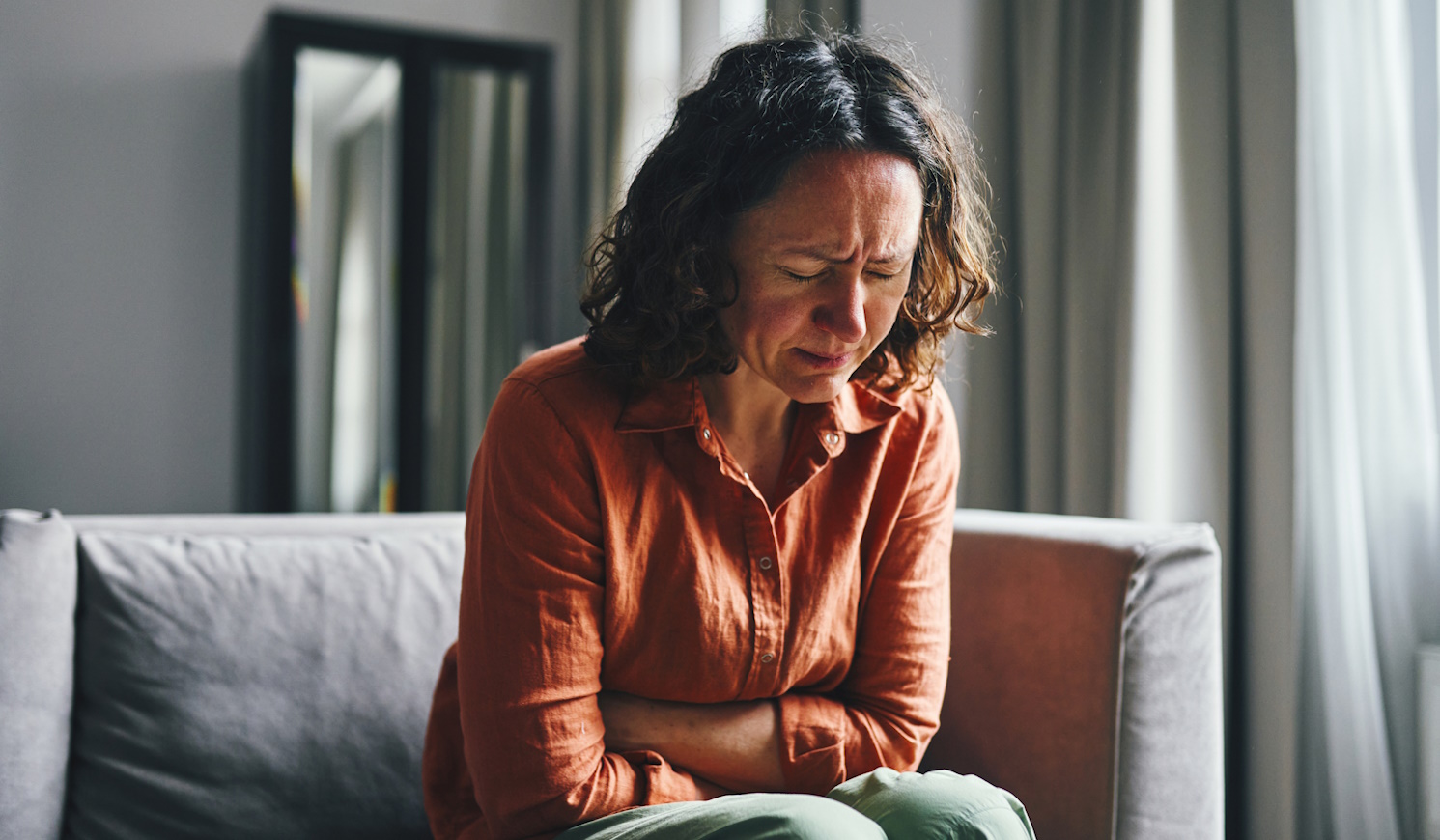 nő görnyed a kanapén, mert fáj a hasa