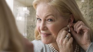 Egy szőke nő gyöngysorral a nyakában rakja be a fülbevalóját