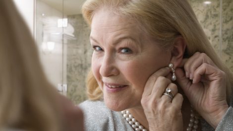 Egy szőke nő gyöngysorral a nyakában rakja be a fülbevalóját