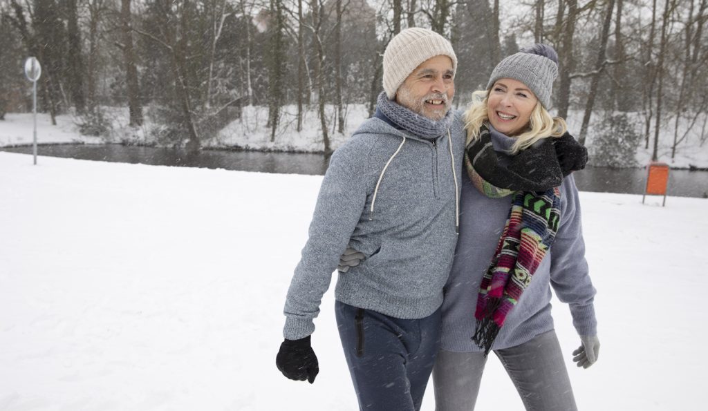 középkorú férfi és nő a hóban sétál boldogan