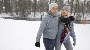 középkorú férfi és nő a hóban sétál boldogan