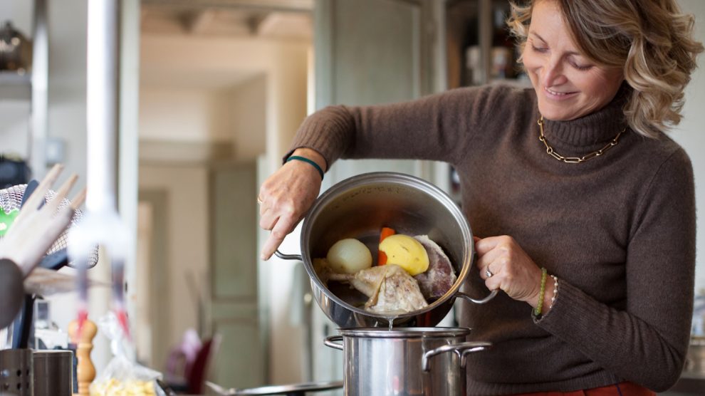 középkorú háziasszony leönti a húsleves első főzővizét