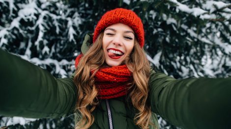 fiatal lány piros sapkában szelfizik a havas háttérrel