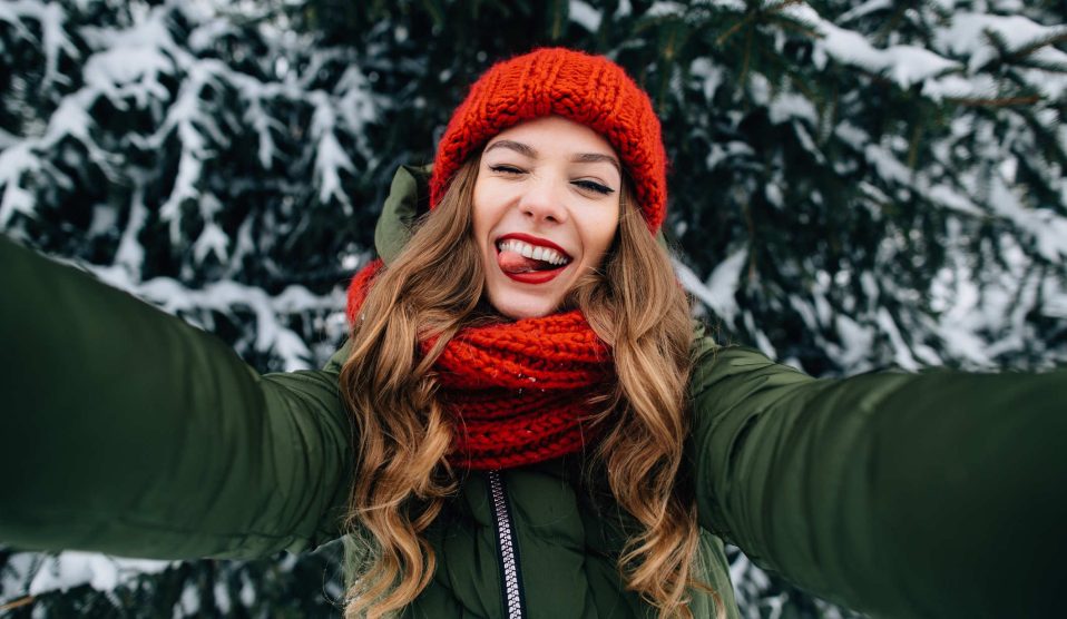 fiatal lány piros sapkában szelfizik a havas háttérrel