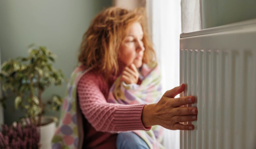 A hideg radiátort fogja egy nő otthon fázik
