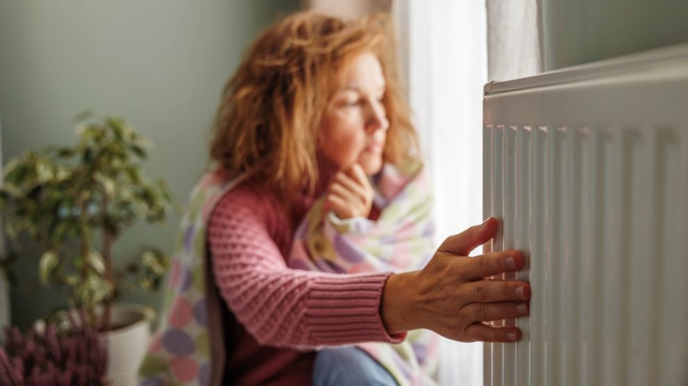 A hideg radiátort fogja egy nő otthon fázik