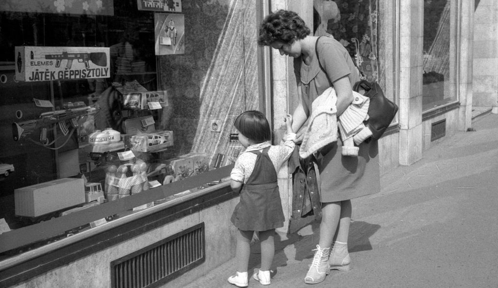 gyerekjátékokat nézeget a kirakatban egy anyuka és kislánya az 1980-as években retró fotó