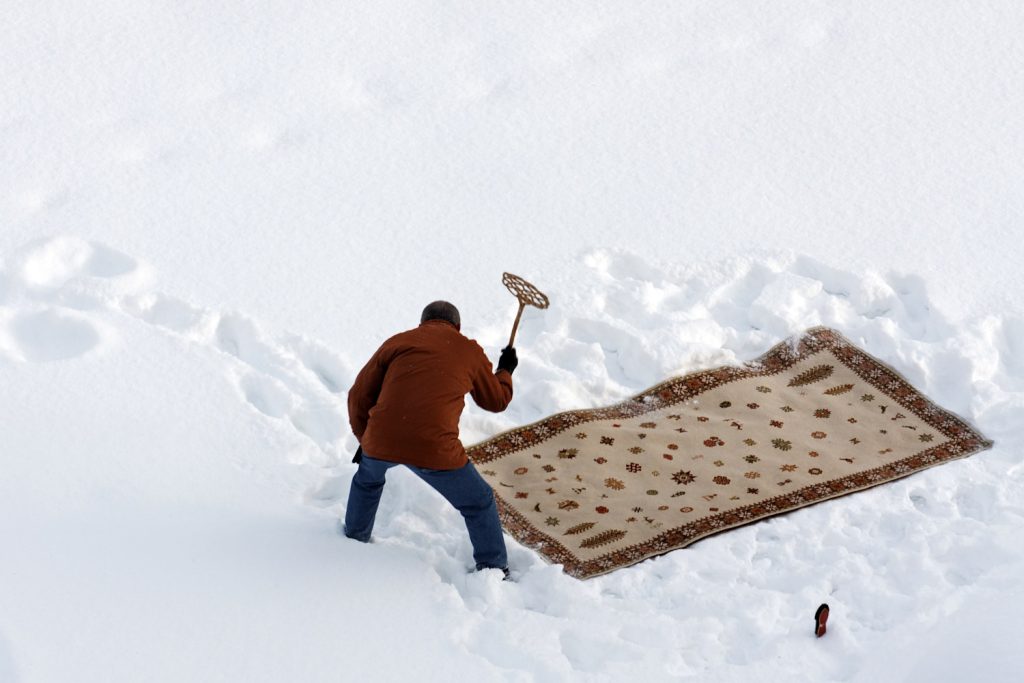 nő szőnyeget takarít hóval