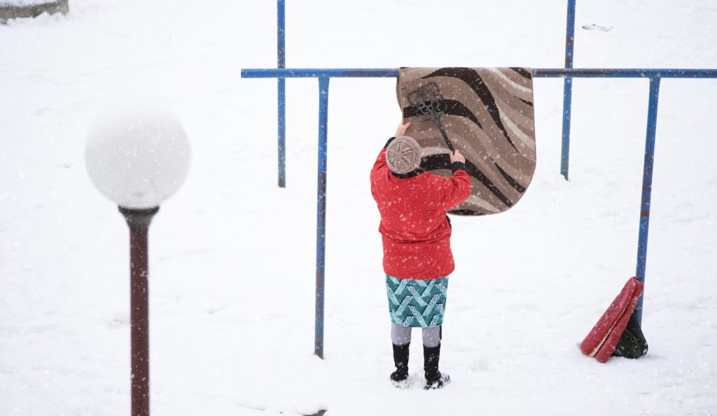 nő szőnyeget takarít hóval