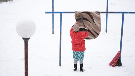 nő szőnyeget takarít hóval