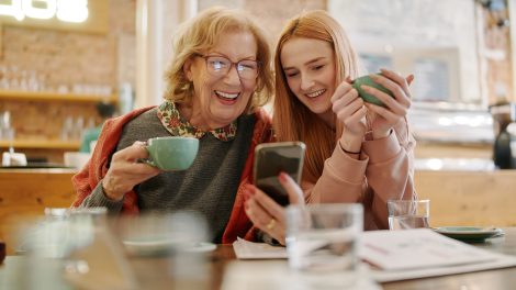 Nagymama az unokájával kávézniak és nézik a telefont