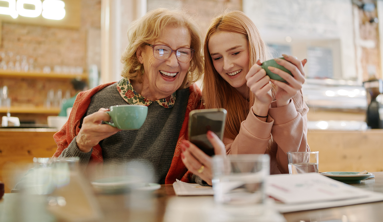 Nagymama az unokájával kávézniak és nézik a telefont