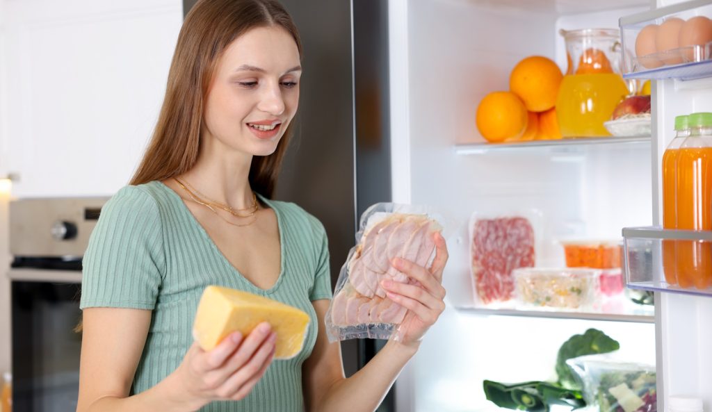 sajtot és felvágottat pakol a hűtőbe egy fiatal nő