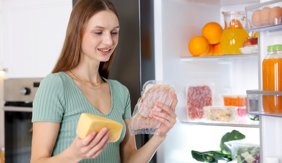 sajtot és felvágottat pakol a hűtőbe egy fiatal nő