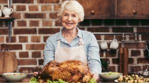 szép idős hölgy a konyhában egy egész grillcsirkével